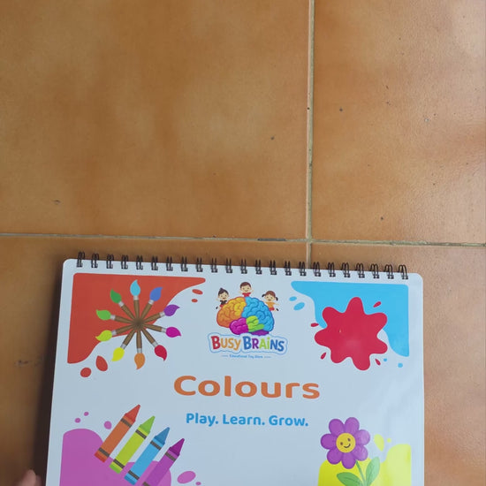 Toddler flipping through Busy Brains Colours Activity Binder with Montessori learning pages